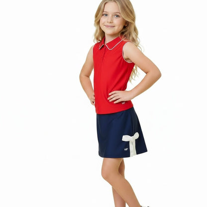 Girl wearing navy athletic skirt with white bow detail and red top on white background