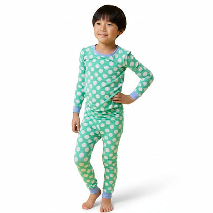 A young child modeling a two-piece long-sleeve pajama set with a mint green and white golf ball on tee pattern, featuring light blue ribbed cuffs and collar, on a white studio background.