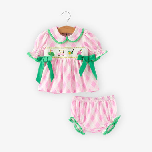 Front view of pink smocked baby outfit with embroidered golf icons, green bows, and matching bloomers
