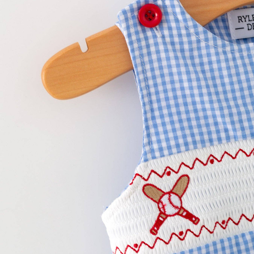Close-up of blue plaid baby romper with smocked baseball embroidery and red button shoulder detail